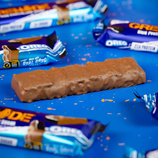 Ein einzelner Grenade Oreo Proteinriegel ohne Verpackung liegt auf einem Tisch. Der Riegel zeigt seine glatte, schokoladige Außenseite.