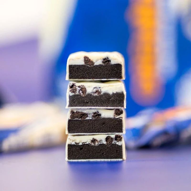 Vier gestapelte, durchgeschnittene Grenade Proteinriegel Oreo White ohne Verpackung, die die schichtweise Struktur mit weißer Schokolade und OREO-Stückchen zeigen.