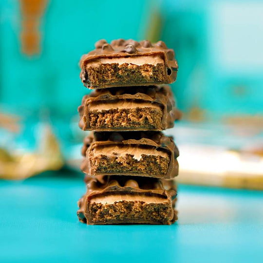 Vier gestapelte Grenade Protein Riegel Chocolate Chip Salted Caramel, in der Mitte durchgeschnitten, um die Schichten aus Eiweiß-Nougat, Salzkaramell und Vollmilchschokolade zu zeigen.