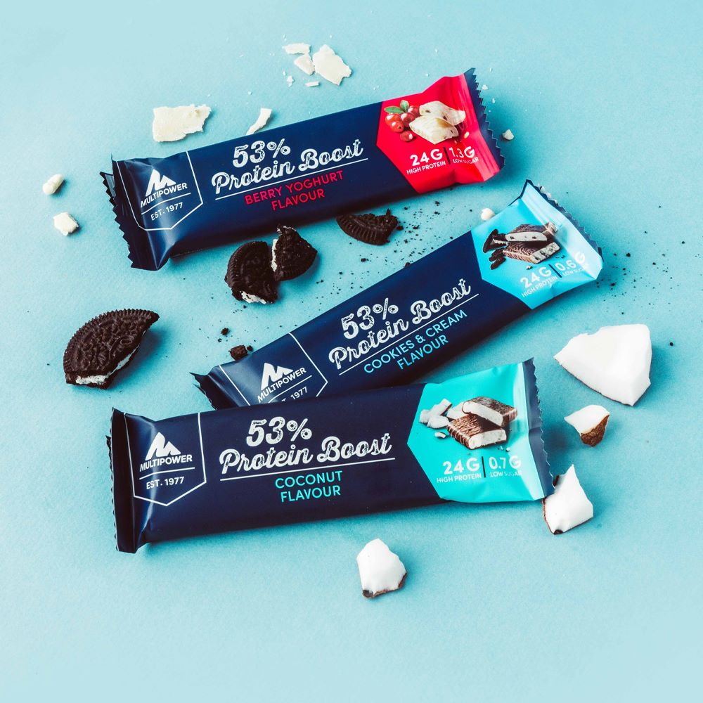 Alle Sorten der Protein Boost Riegel auf einen blauen Hintergrund mit einzelnen Stückchen der Riegelzutaten daneben.
