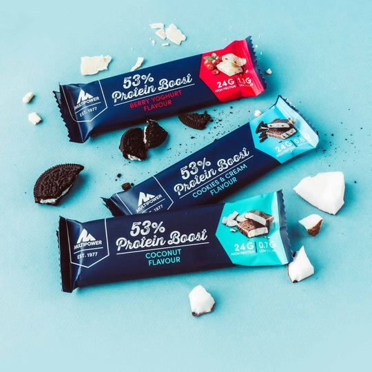 Alle Sorten der Protein Boost Riegel auf einen blauen Hintergrund mit einzelnen Stückchen der Riegelzutaten daneben.