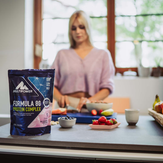 Multipower Formula 80 Beutel und im Hintergrund schneidet eine Frau einen Riegel