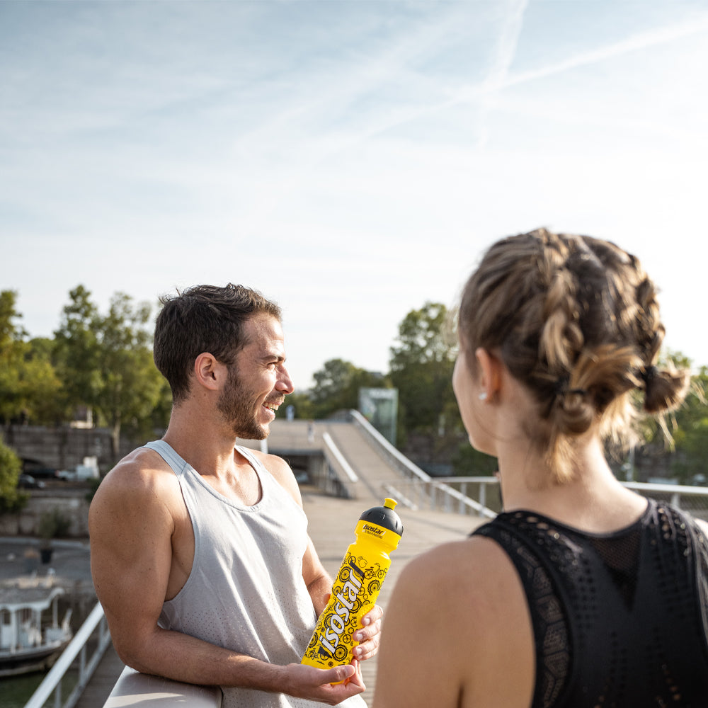 Mann und Frau machen eine Pause auf einer Brücke mit Isostar Flasche
