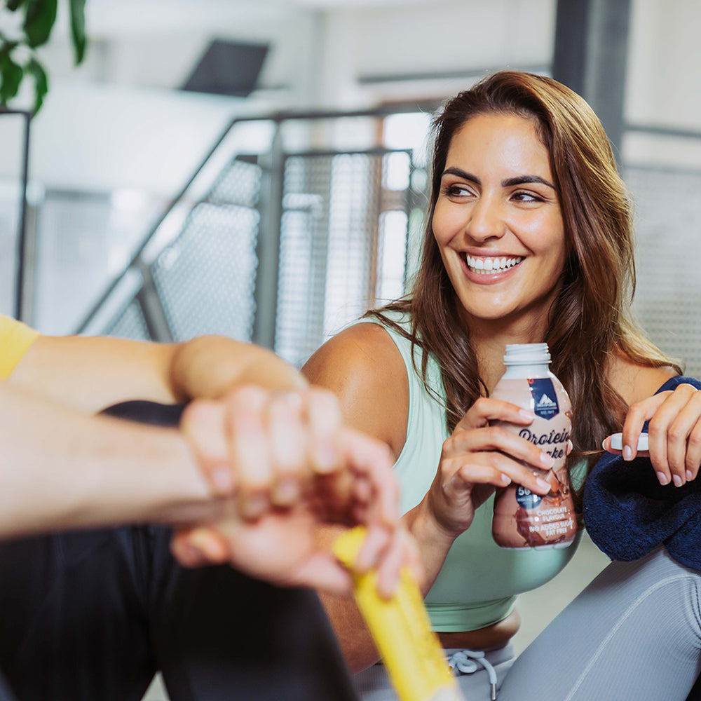 Eine Frau lächelt und hält einen Protein Shake von Multipower in der Hand